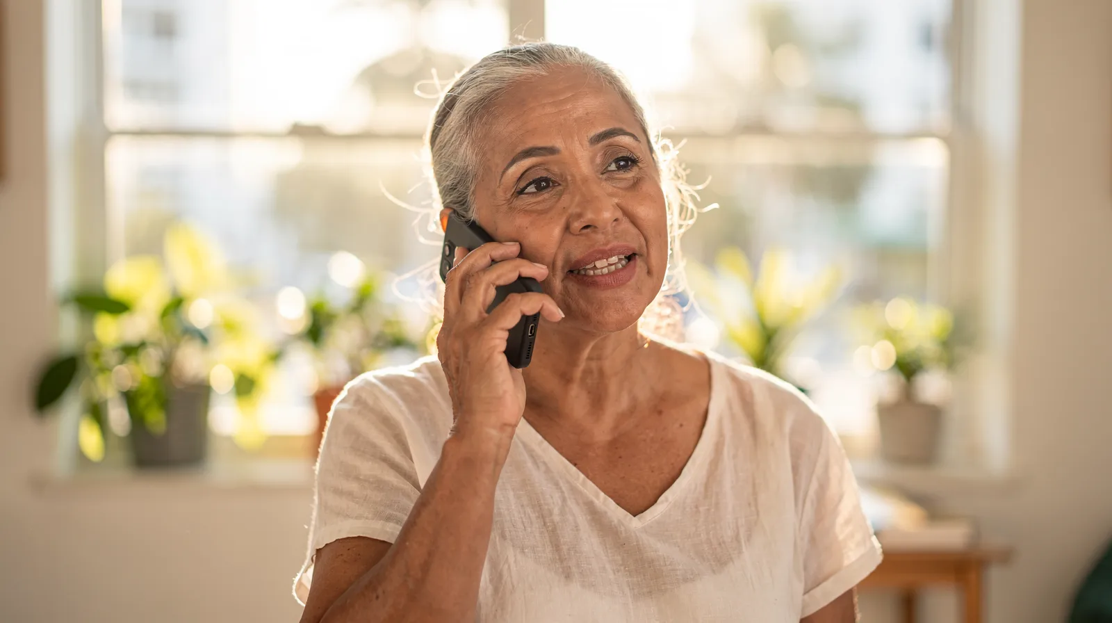 A woman in her sixties talking on her phone at home in warm afternoon light