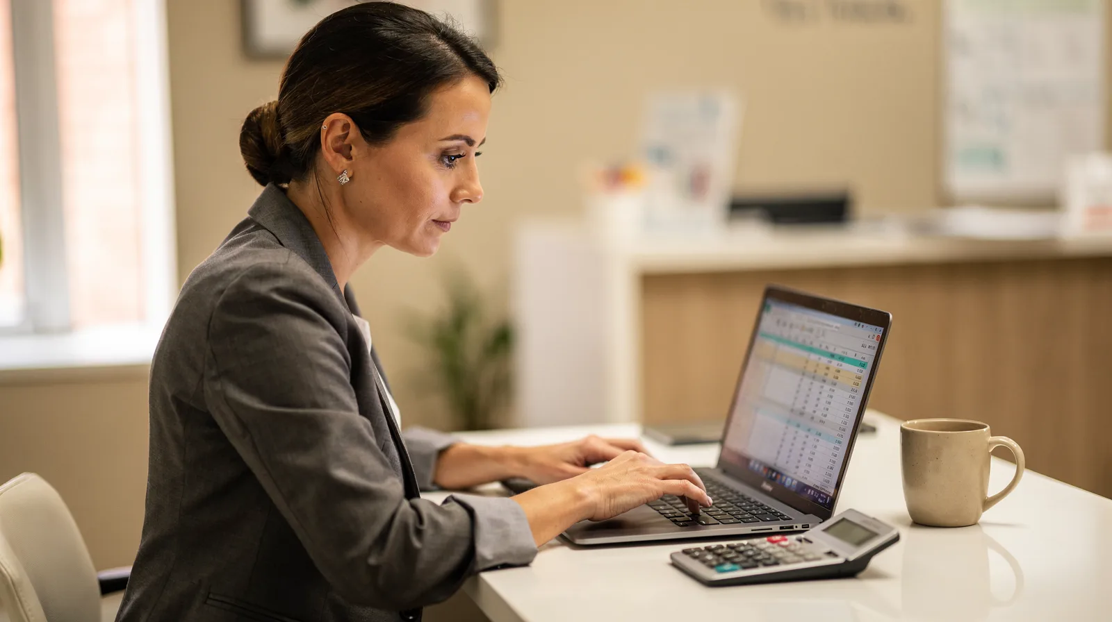 A practice manager reviewing a monthly budget on a laptop at a clinic front desk