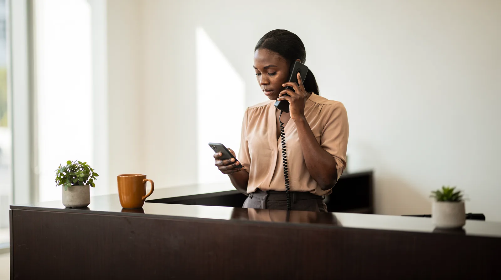 A front desk coordinator answering a desk phone while checking her mobile phone